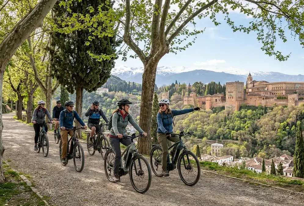 Cyclists on e-bikes riding through the narrow cobbled streets of the Albaicín quarter in Granada with the Alhambra visible on the hill behind
