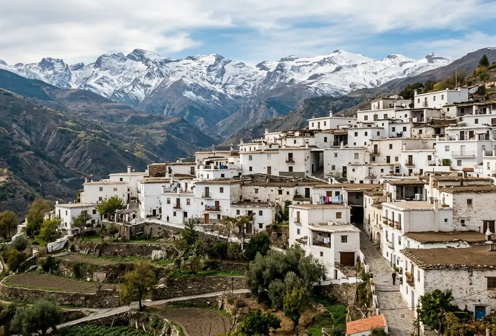The white launa-roofed village of Capileira in the Alpujarras above Granada, flat terraces and tinaos on a mountain hillside, Sierra Nevada peaks behind, illustrating the Morisco architectural legacy of the moriscos granada history expulsion